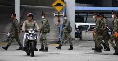 A motorcyclist rides past soldiers wearing face masks inside a police station during the control of movement in Kuala Lumpur amid fears over the spread of the coronavirus, Sunday, March 22, 2020. (AFP Photo)