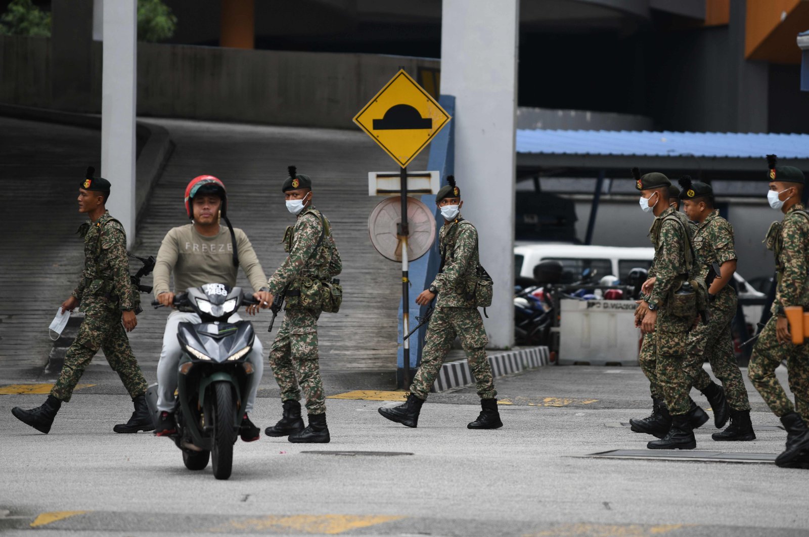 A motorcyclist rides past soldiers wearing face masks inside a police station during the control of movement in Kuala Lumpur amid fears over the spread of the coronavirus, Sunday, March 22, 2020. (AFP Photo)