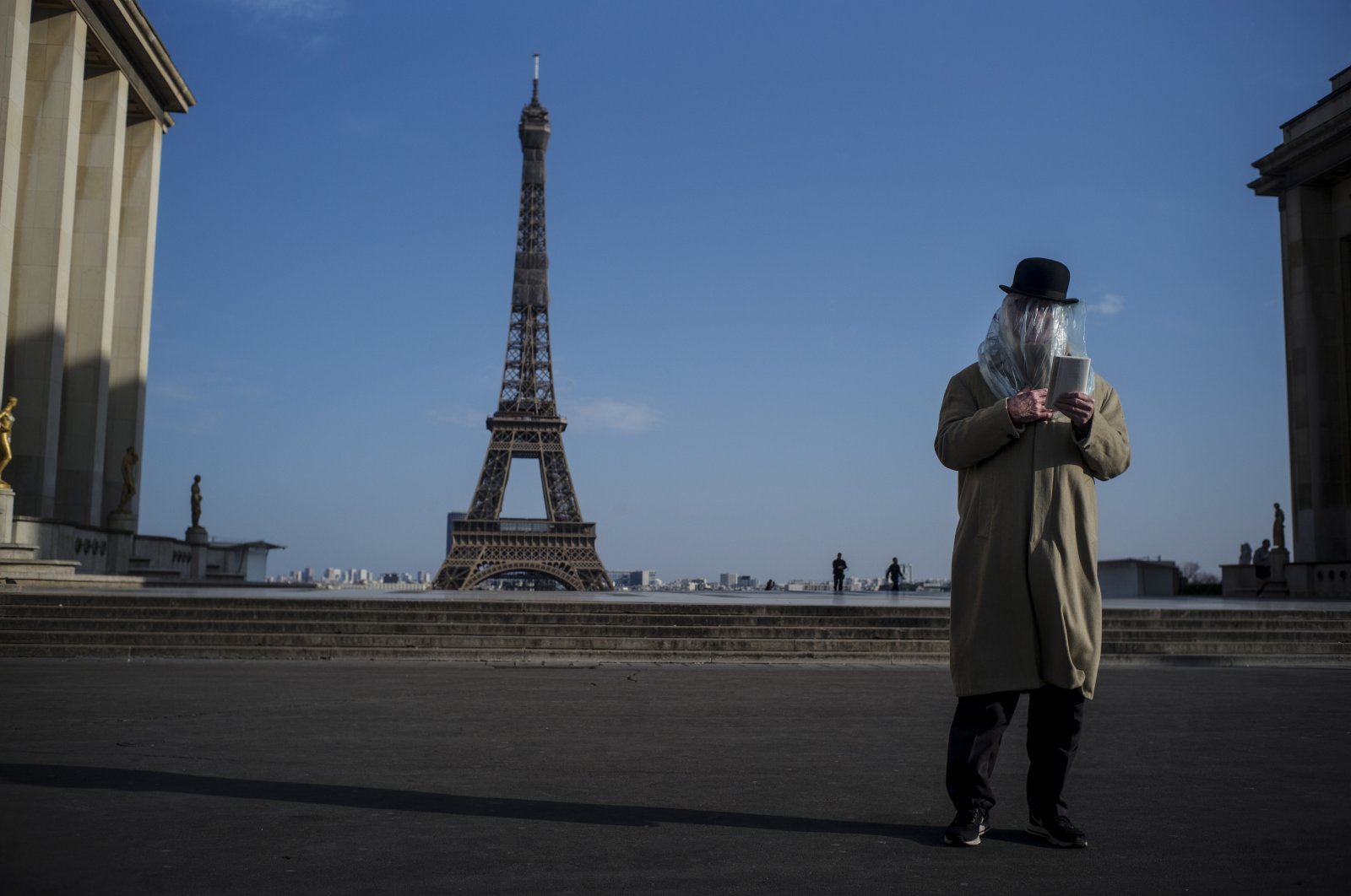 A man has his head covered with a plastic bag for protection reads a book in front of the Eiffel tower in Paris, France, 22 March 2020. (EPA Photo)