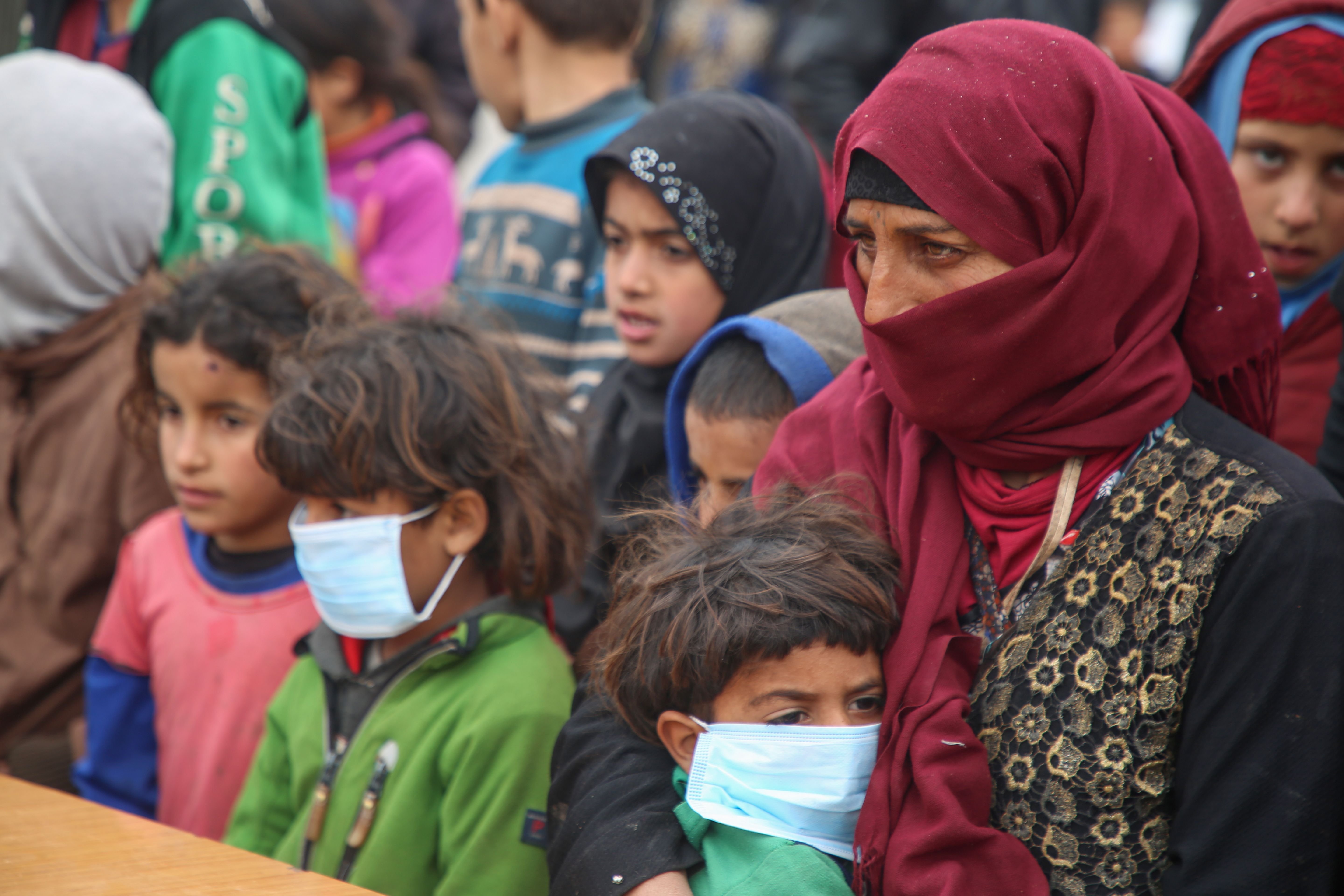 Displaced Syrians, some wearing protective masks, listen as medics hold an awareness campaign on how to be protected against the coronavirus pandemic in a camp for displaced people in Kafr Lusin, in the northwestern province of Idlib, following heavy storms, Wednesday, March 18, 2020. (AFP Photo)