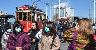 Tourists wear protective face masks as they walk at Taksim Square as the nation tries to limit the spread of the new coronavirus, in Istanbul, Tuesday, March 17, 2020. (AFP Photo)