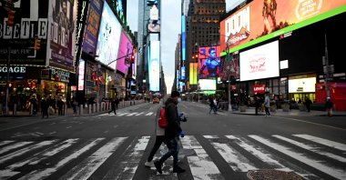 People wearing masks cross the street in Times Square in Manhattan, New York City, Tuesday, March 17, 2020. (AFP Photo)