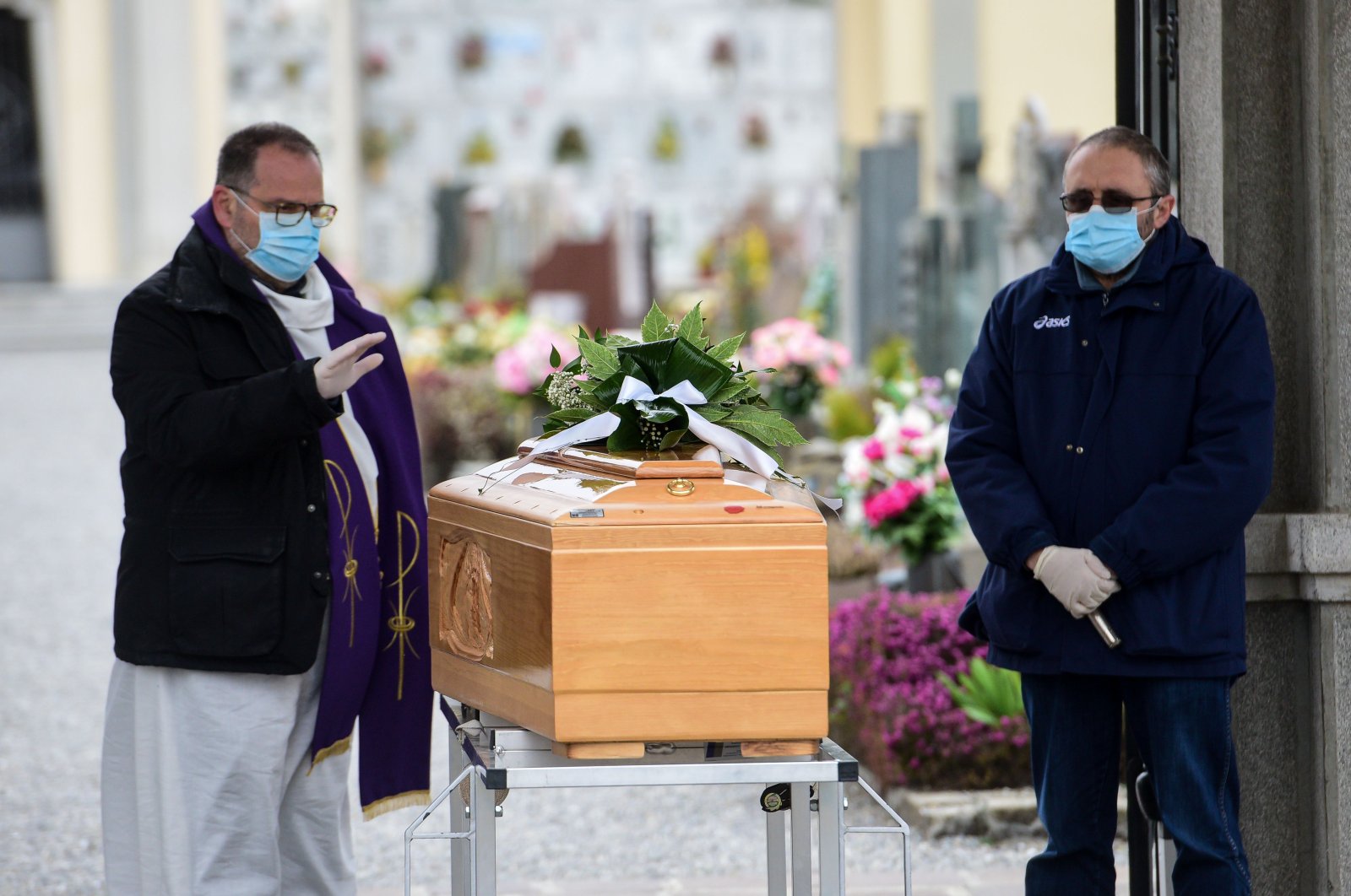 A priest (L), assisted by a pallbearer, both wearing a face mask, gives the last blessing to a deceased person, by a coffin during a funeral service at the cemetery of Bolgare, Lombardy, on March 23, 2020 during the COVID-19 new coronavirus pandemic. (AFP Photo)