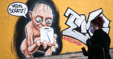 A woman walks in front of graffiti depicting the character of Gollum from "Lord of the Rings," holding a roll of toilet paper and saying "My precious," in the Mauerpark public park in the Prenzlauer Berg district of Berlin, Germany, Saturday, March 21, 2020. (AP Photo)