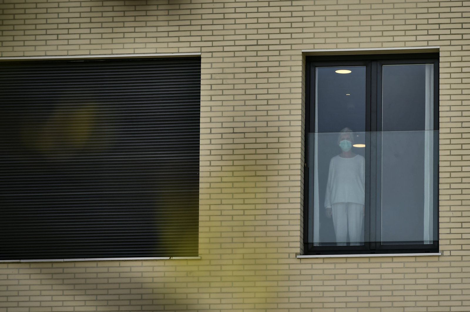 An elderly woman wearing a protective mask looks on through the window at San Martin nursing home, Vitoria, Thursday, March 19, 2020. (AP Photo)