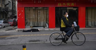 An elderly man wearing a face mask who collapsed and died lays on a street near a hospital as another man rides a bicycle past him in Wuhan, China, Jan. 30, 2020. (AFP Photo)
