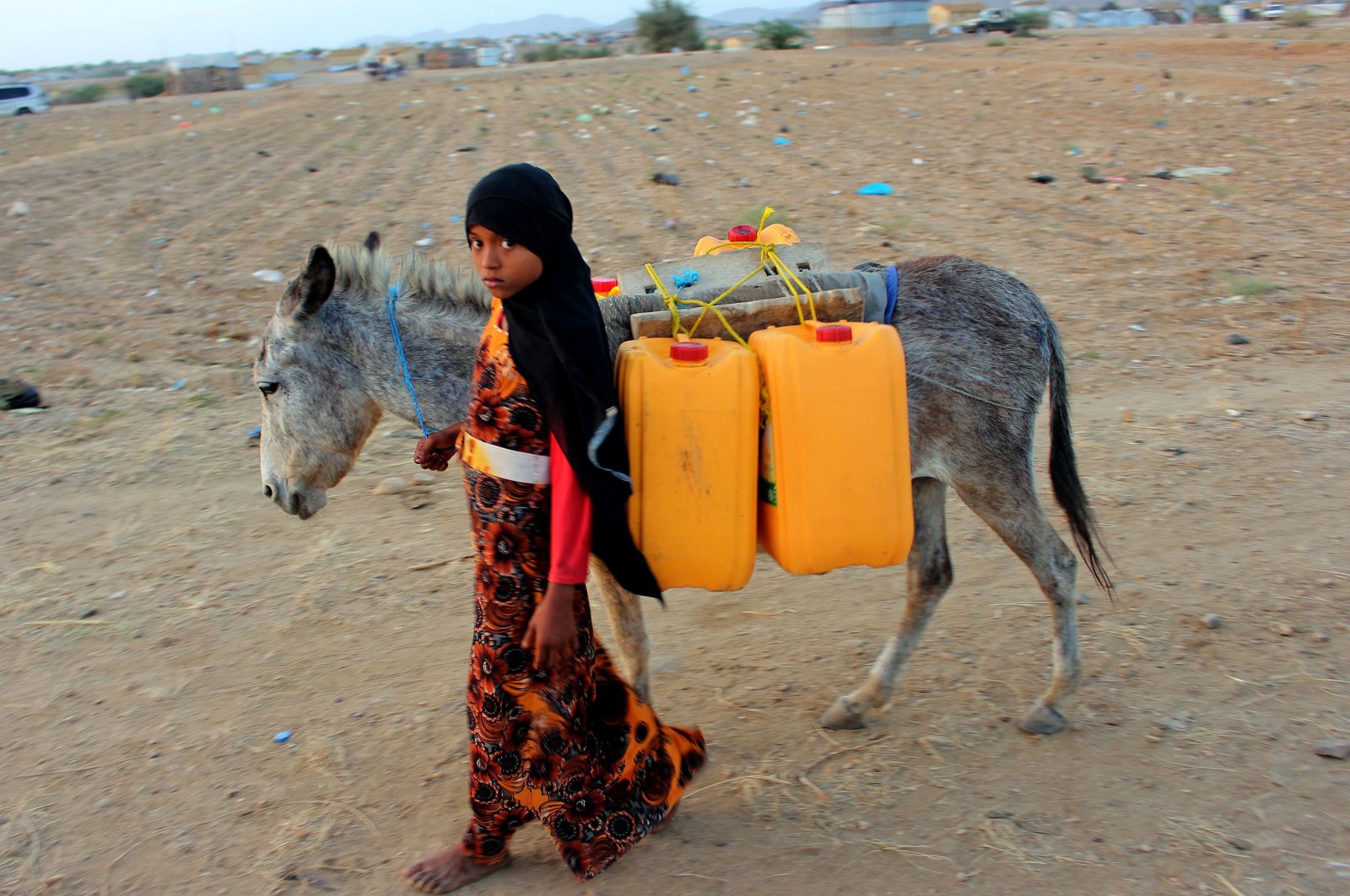 A girl walks with a donkey carrying jerrycans filled with water from a cistern at a makeshift camp for displaced Yemenis with a severe shortage of water, in the northern Hajjah province,Tuesday, March 24, 2020. (AFP Photo)