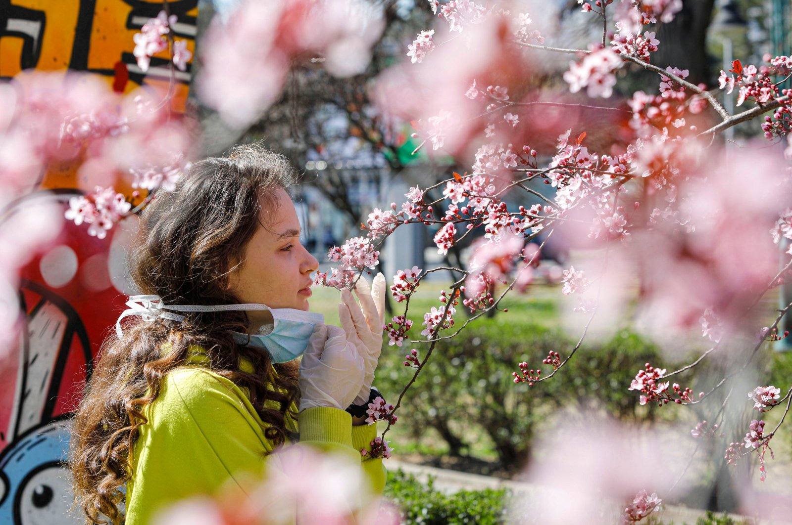 A girl removes her mask to smell the flowers on a blooming tree in Skopje, North Macedonia, Friday, March 20, 2020. (Reuters Photo)