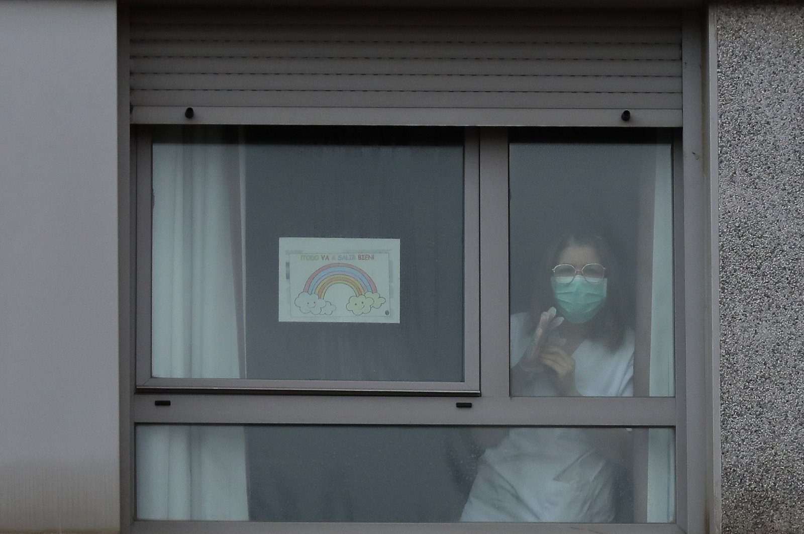 A nurse looks out from a window next to a banner reading in Spanish "Everything is going to be all right" inside of a nursing homes, Madrid, Tuesday, March 24, 2020. (AP Photo)