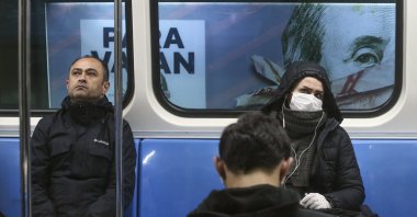 Commuters in an underground train, some wearing masks, are driven past a billboard of a book advertisement featuring a picture of U.S. President Benjamin Franklin on the $100 bill, in Istanbul, Turkey, Wednesday, March 25, 2020. (AP Photo)