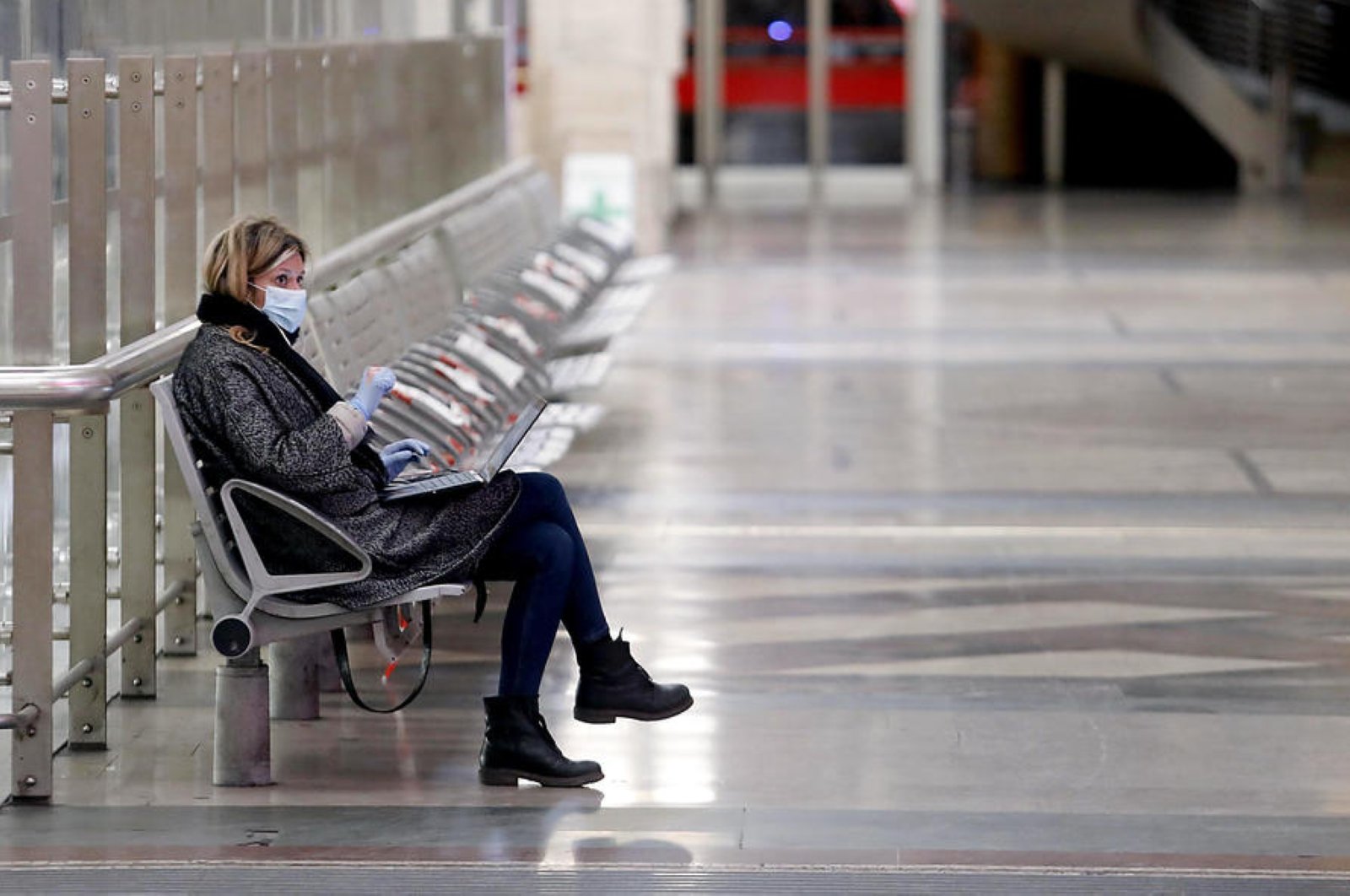 A woman wearing a face protective masks sits at Milan Central Station, Milan, Italy, Wednesday, March 25, 2020. (EPA Photo)