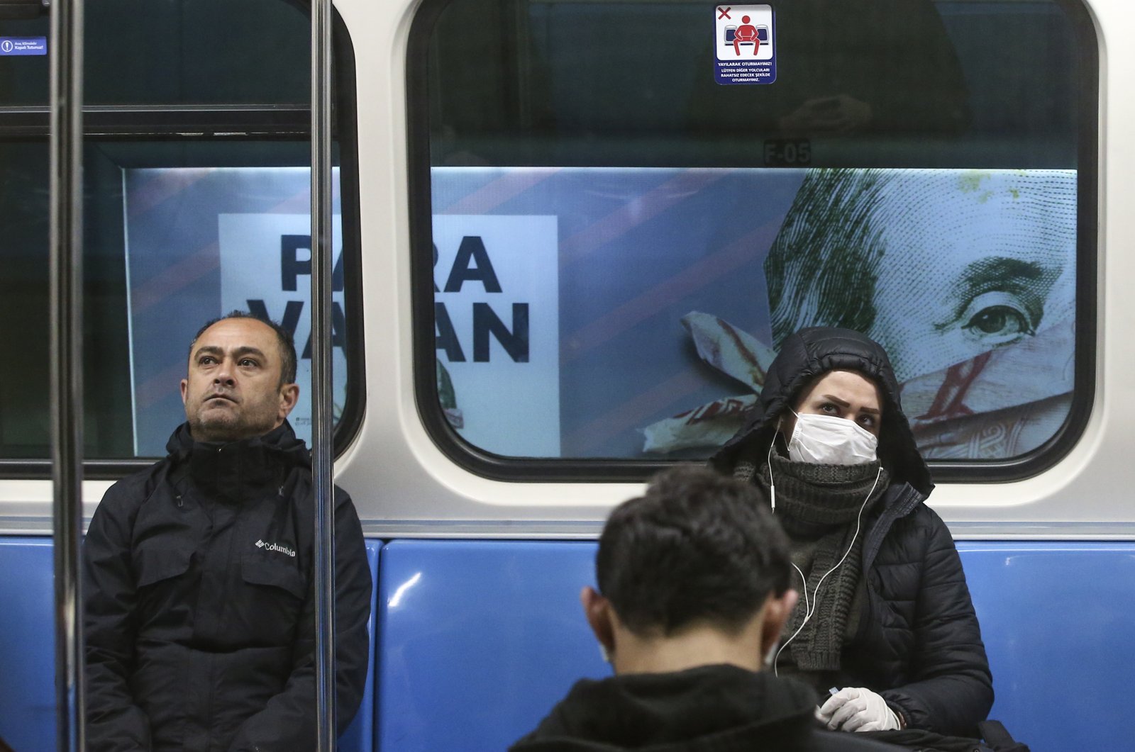 Commuters in an underground train, some wearing masks, are driven past a billboard of a book advertisement featuring a picture of U.S. President Benjamin Franklin on the $100 bill, in Istanbul, Turkey, Wednesday, March 25, 2020. (AP Photo)