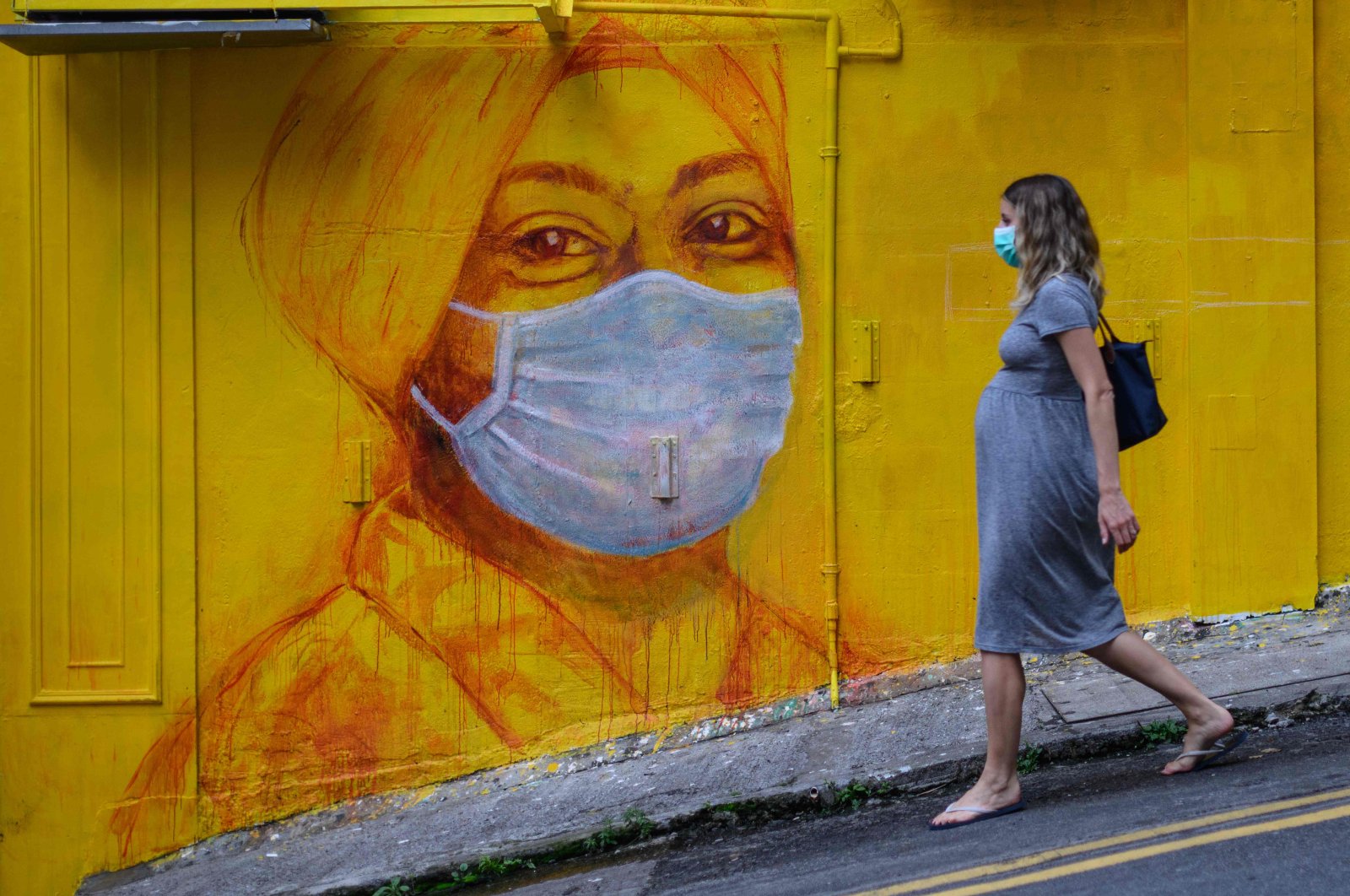 A pregnant woman wearing a face mask walks past a street mural in Hong Kong, March 23, 2020.