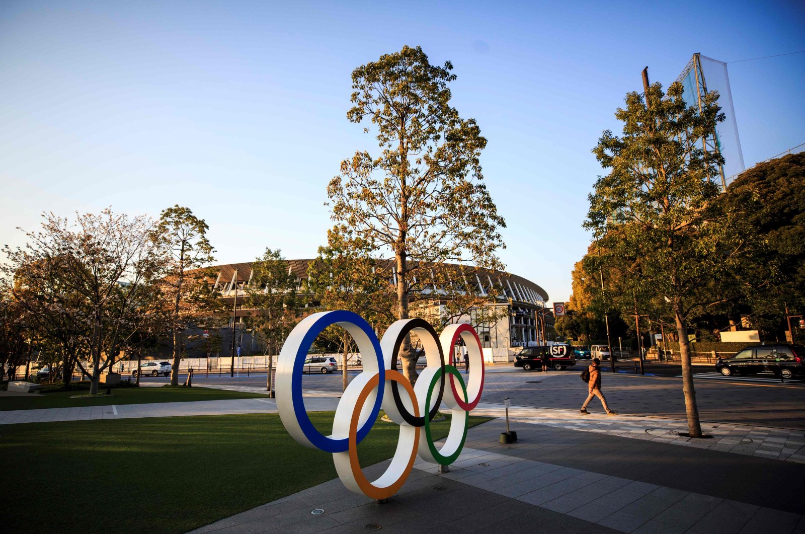 A man walks past the Olympic rings in front of the Japan National Stadium, the main venue for the Tokyo 2020 Olympic Games, in Tokyo, Japan, Wednesday, March 25, 2020. (AFP Photo)