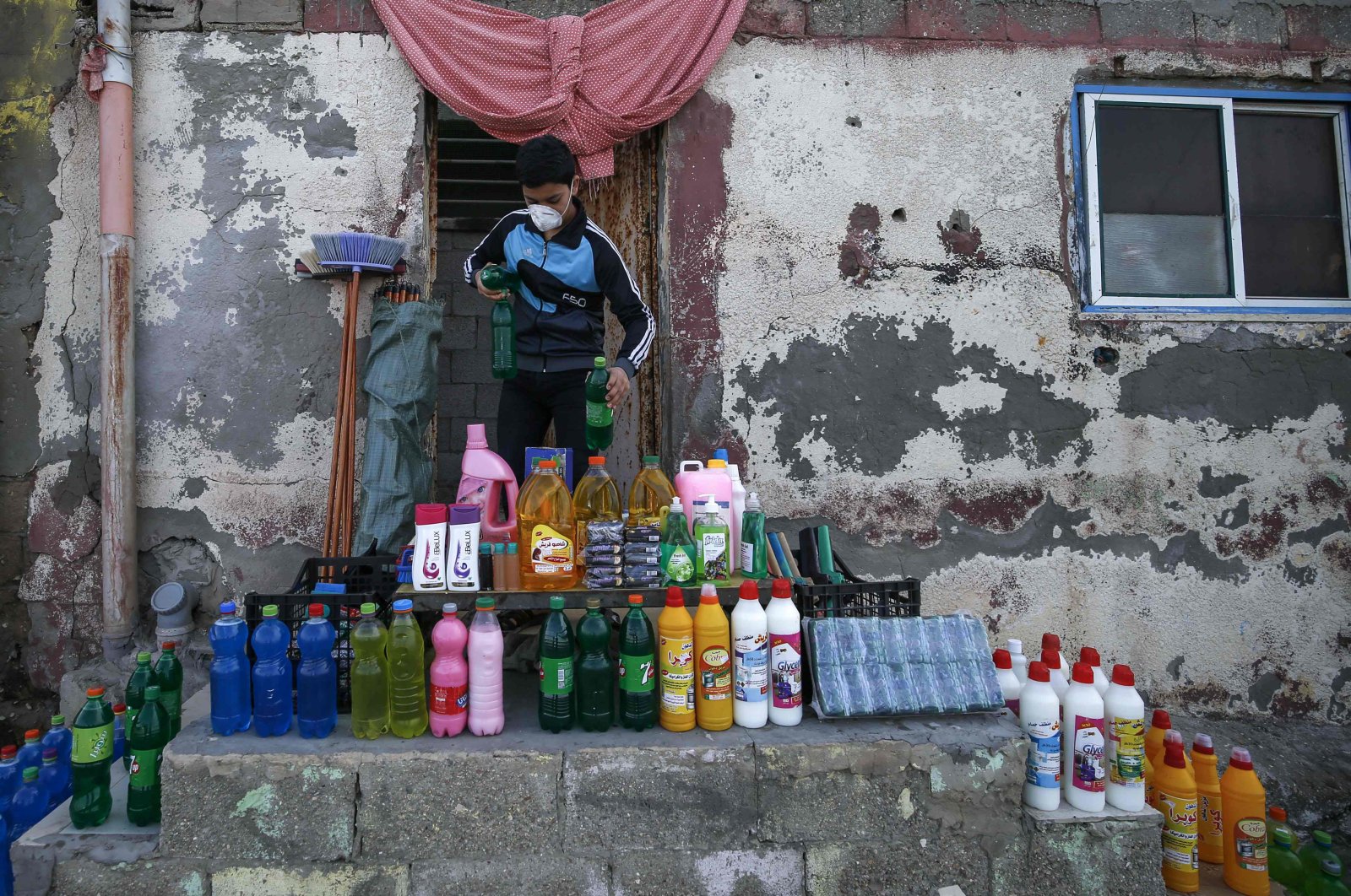 A Palestinian boy wearing a protective mask sets cleaning tools and disinfectants for sale in front of his home in al-Shati refugee camp, Thursday, March 26, 2020. (AFP Photo)