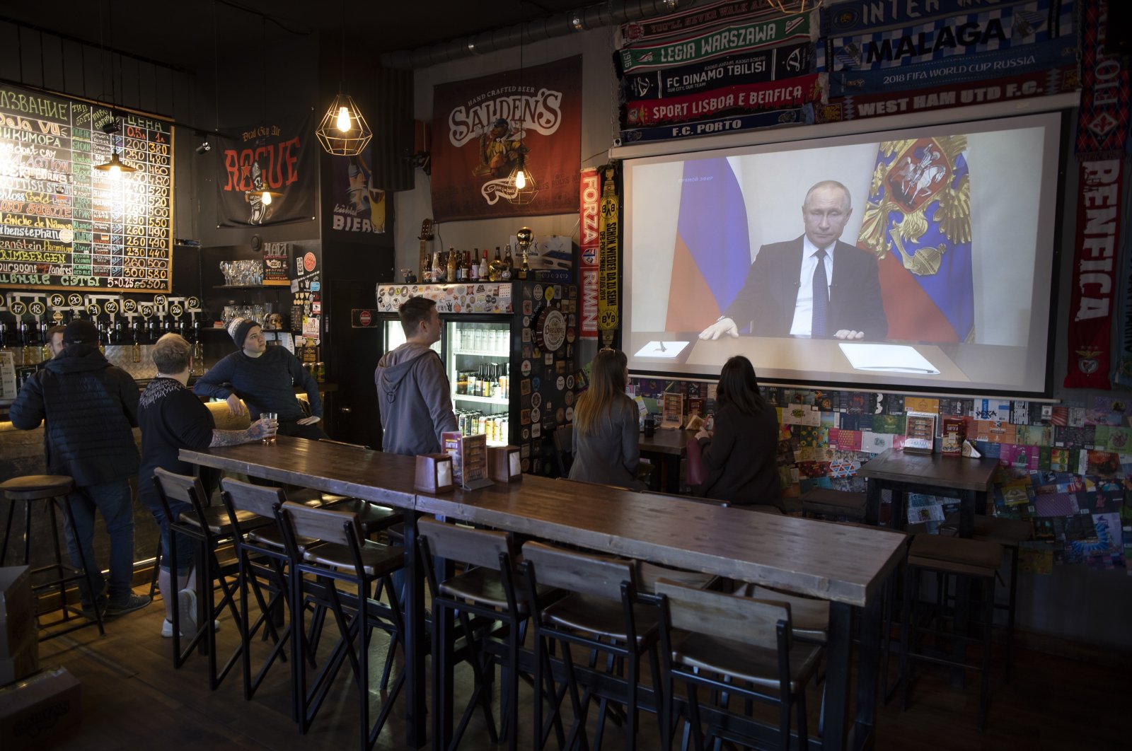 A few visitors and staff of a pub watch the broadcast of Russian President Vladimir Putin addressing Russian citizens on the state television channel in Moscow, Russia, Wednesday, March 25, 2020. (AP Photo)