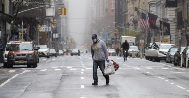 A man wearing a face mask walks across the middle of 5th Avenue in Midtown Manhattan, New York City, Sunday, March 29, 2020. (AP Photo)