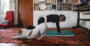 This picture taken on March 23, 2020 shows a woman taking part in an online pilates class at home, as her dog Elvis stretches next to her, in Nicosia. (AFP Photo)