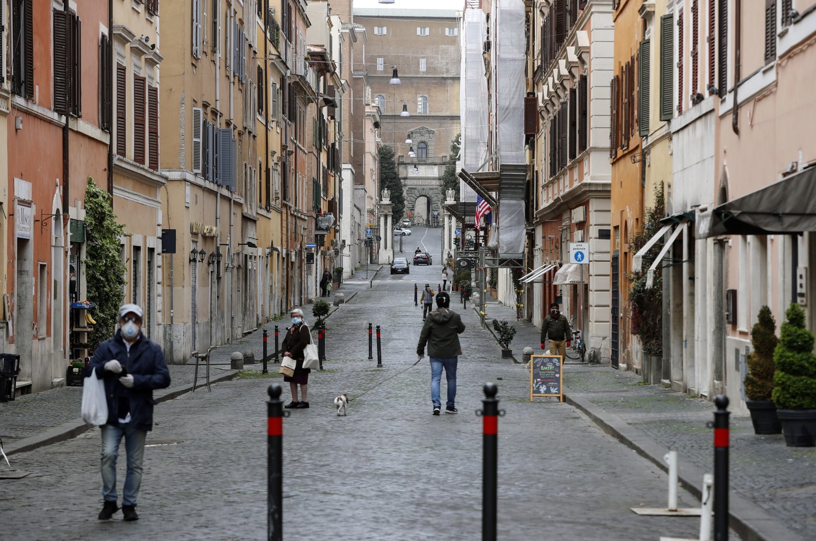 People wearing face masks walk on a street, during the coronavirus lockdown in Rome, in Borgo Pio, Italy, Monday, March 30, 2020. (EPA Photo)