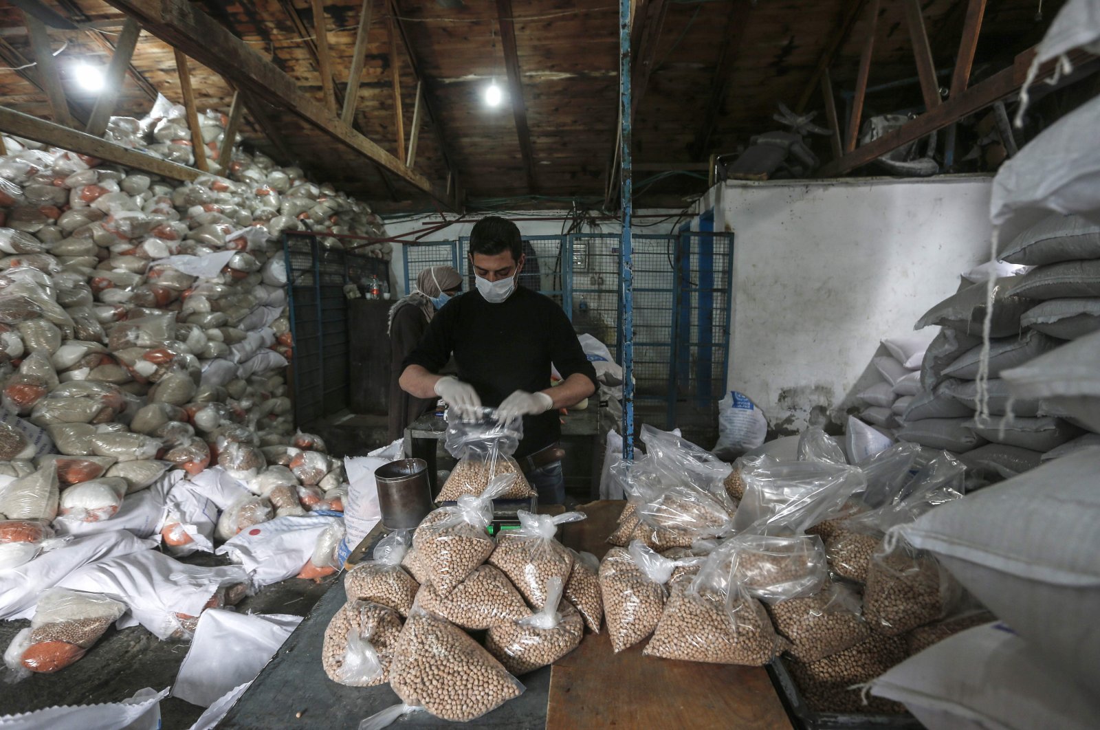 Palestinian employees at the United Nations Relief and Works Agency for Palestinian Refugees (UNRWA) wearing protective masks and gloves prepare food aid rations to be delivered to refugee family homes rather than distributed at a U.N. center, in Gaza City, Tuesday, March 31, 2020. (AFP Photo)