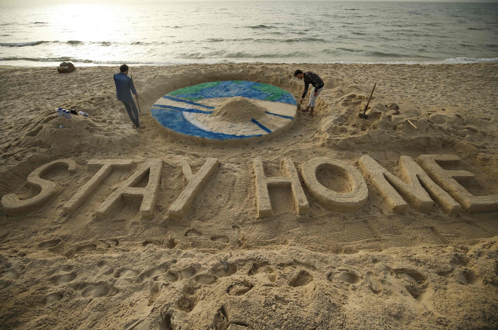 Palestinian artists work on a sand sculpture depicting the earth with a message reading "Stay Home" along a beach in Gaza City during the COVID-19 coronavirus pandemic, Tuesday, March 31, 2020. (AFP Photo)