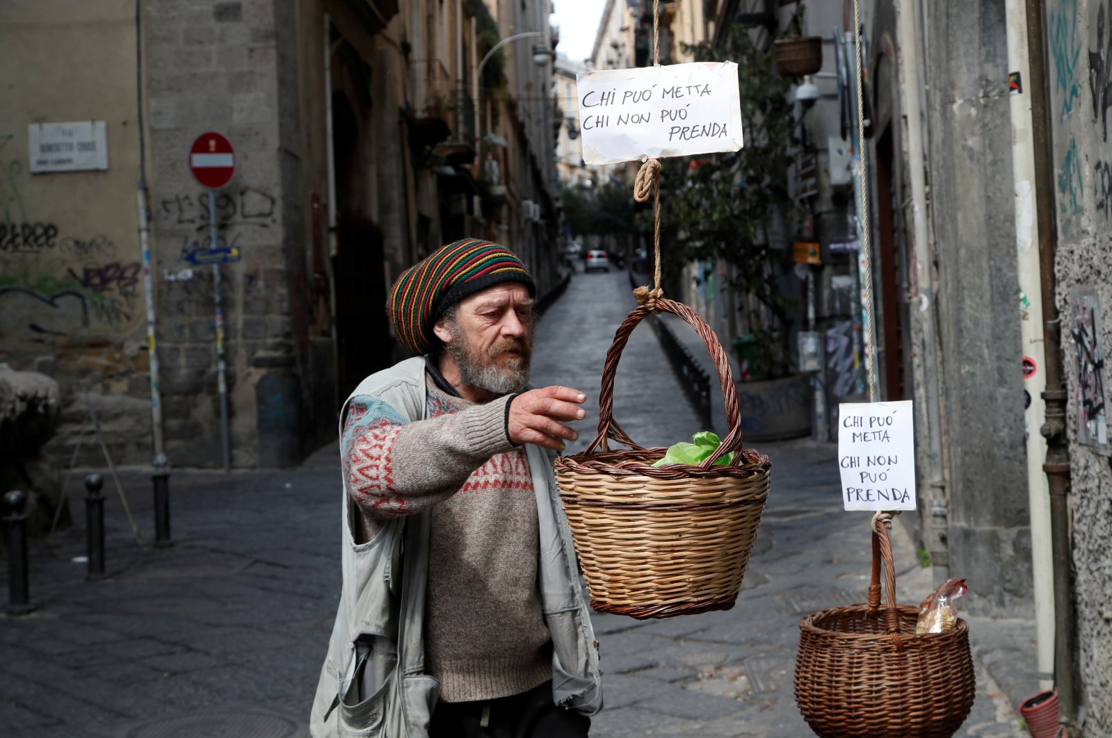 A man reaches to a basket that was hung up so people can donate or take free food, as Italy struggles to contain the spread of the coronavirus, in Naples, Italy, Monday, March 30, 2020. The sign reads: "Who can puts in, who can't takes." (Reuters Photo)