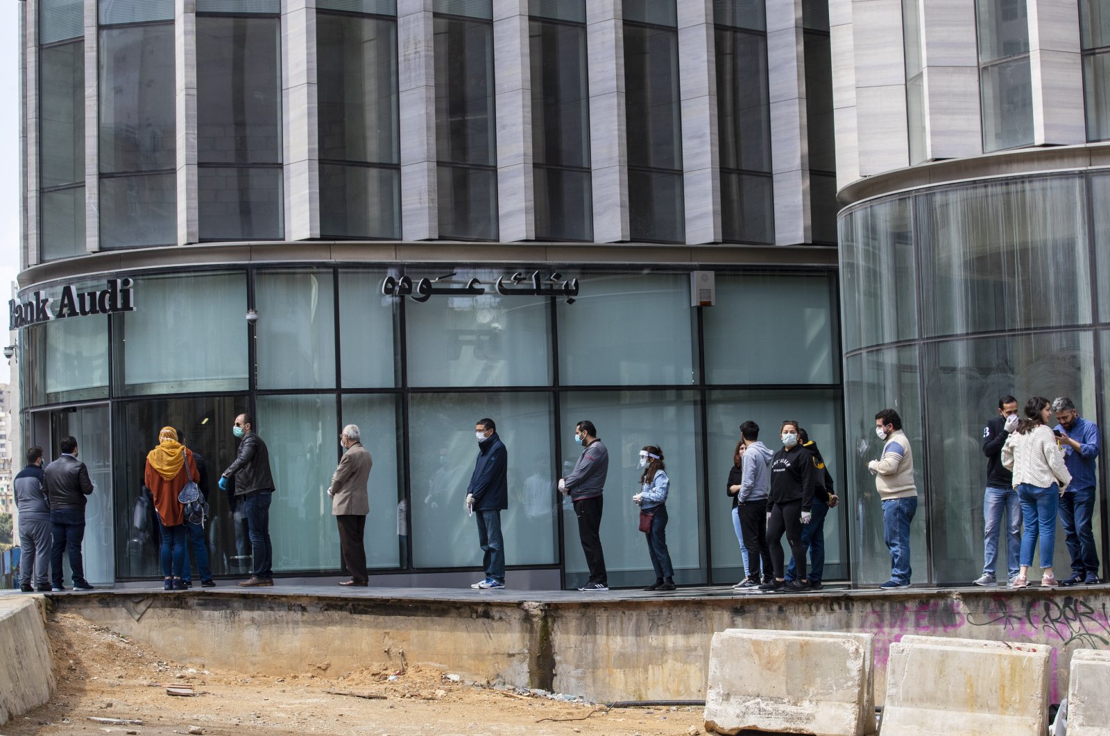 Clients wearing masks to help protect themselves from the coronavirus wait to use ATM machines outside a closed bank in Beirut, Lebanon, Saturday, March 28, 2020. (AP Photo)