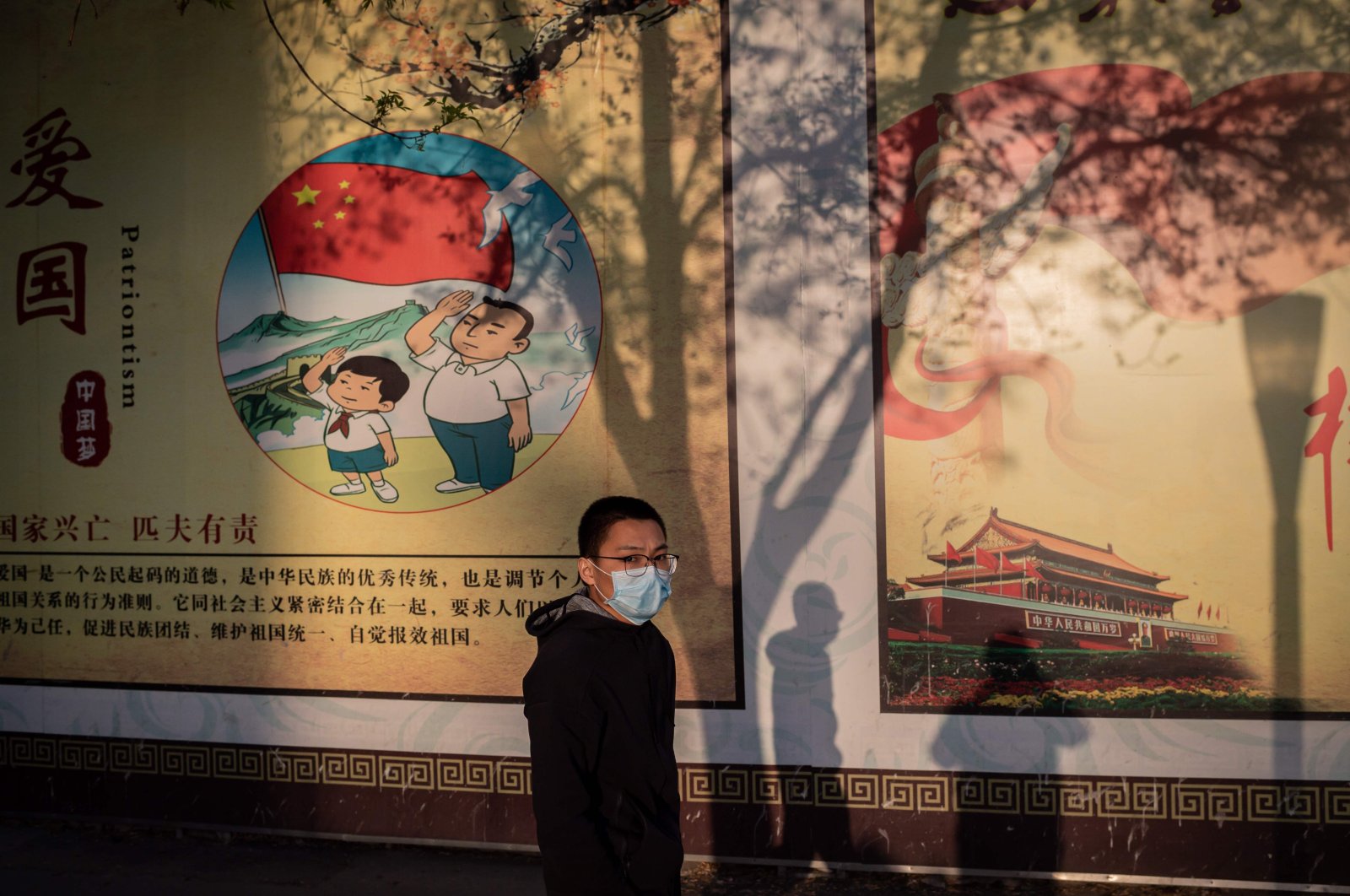 A boy wearing a wearing a facemask as a preventive measure against the COVID-19 coronavirus walks past a propaganda poster outside a shopping mall in Beijing on April 1, 2020. (AFP Photo)