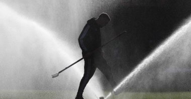A field worker walks through a spray of water on the pitch prior to the start of the Premier League football match between Watford and Tottenham Hotspur at Vicarage Road, Watford, England, Jan. 18, 2020. (AP Photo)