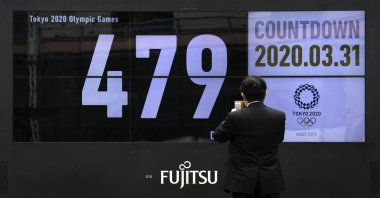 A man takes pictures of a countdown display for the Tokyo 2020 Olympics after it was restarted following the decision to postpone the Games, Tuesday, March 31, 2020, in Tokyo. (AP Photo)