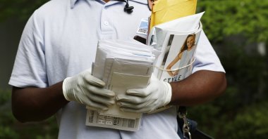 A postal service carrier dons gloves as he delivers mail in northeast Jackson, Miss., Monday, March 30, 2020. (AP Photo)