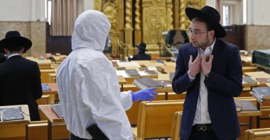 An Israeli police officer, dressed in a protective outfit, speaks to a Yeshiva (Jewish educational institution for studies of traditional religious texts) student, in the Israeli city of Bnei Brak on Thursday, April 2, 2020, during a control to enforce social distancing measures imposed by Israeli authorities to curb the spread of the novel coronavirus. (AFP Photo)