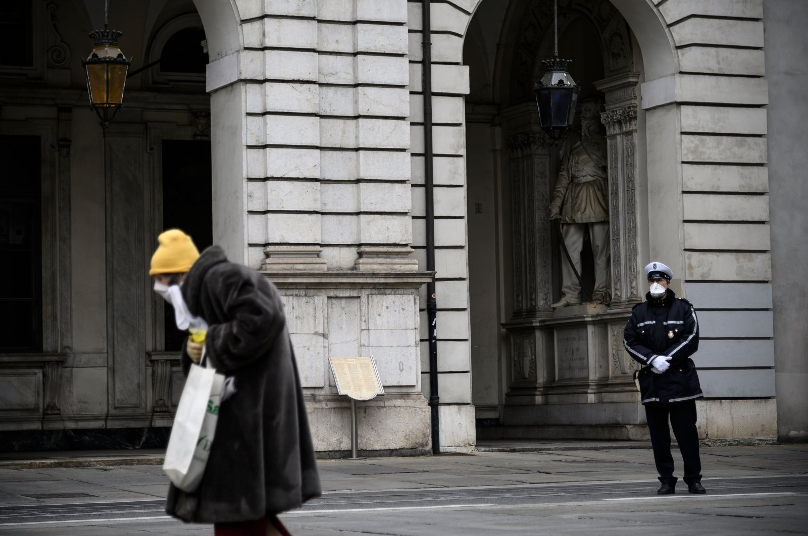 An elderly woman walks past a policeman during a minute of silence at noon in Turin as flags are being flown at half-mast in cities across Italy to commemorate the victims of the virus, Tuesday,  March 31, 2020. (AFP)