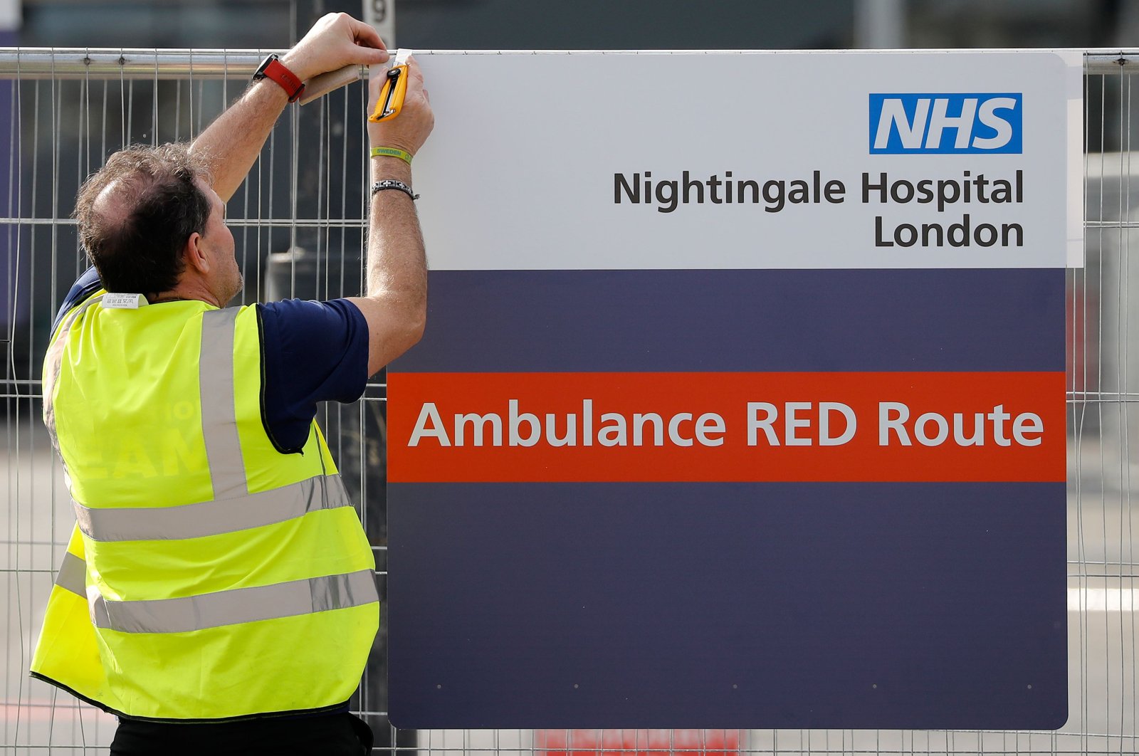 A worker fixes a new sign to a fence at the ExCeL London exhibition center, which has been transformed into the "NHS Nightingale" field hospital, to help with the novel coronavirus COVID-19 pandemic, in London on Friday, April 3, 2020. (AFP Photo)