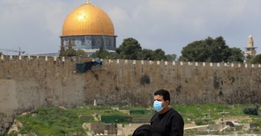 A man wearing a mask and gloves walks past the Dome of the Rock mosqu in Jerusalem's Old City on April 2, 2020. (Photo by Emmanuel DUNAND / AFP)