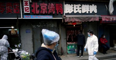 People wearing protective suits walk through a street market in Wuhan, Hubei province, China, Monday, April 6, 2020. (Reuters Photo)