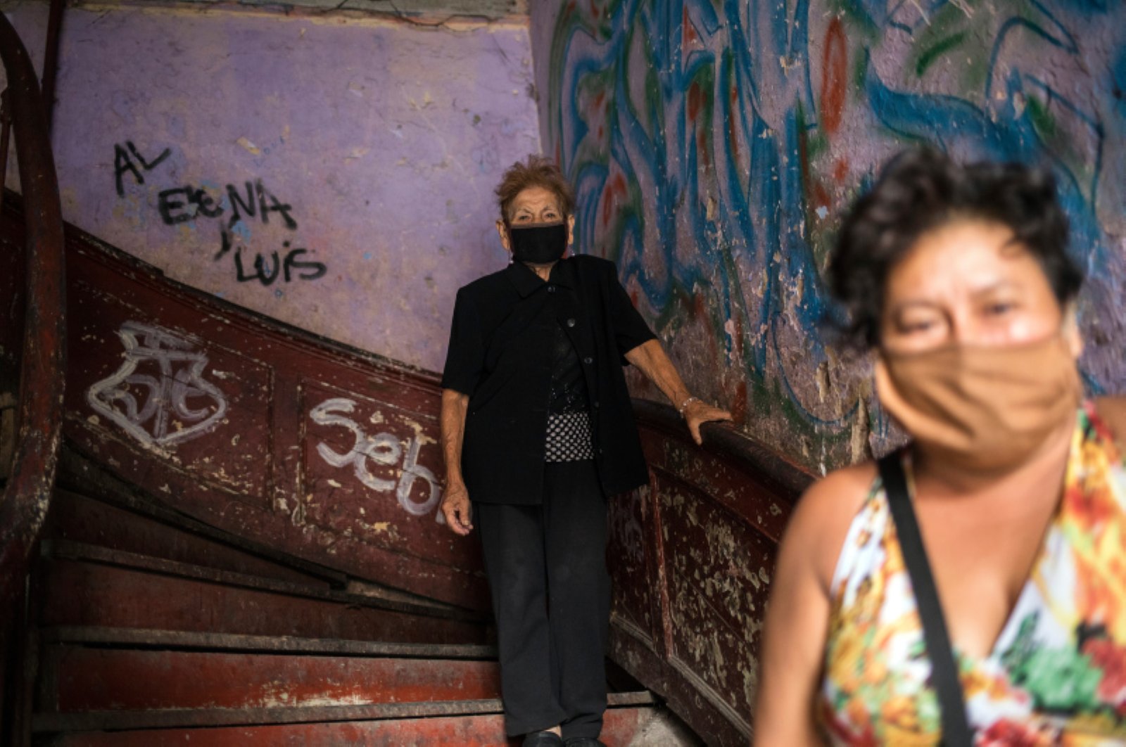 Maria Isabel Aguinaga, 72, wearing a protective face mask, descends the stairs of her crumbling residential building nicknamed “Luriganchito” after the country’s most populous prison, Lima, Peru, March 29, 2020. (AP Photo)