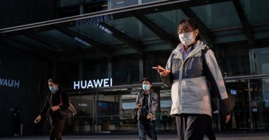 People wearing face masks as a preventive measure against COVID-19 walk outside a shopping mall past a Huawei shop in Beijing, Wednesday, April 1, 2020. (AFP Photo)