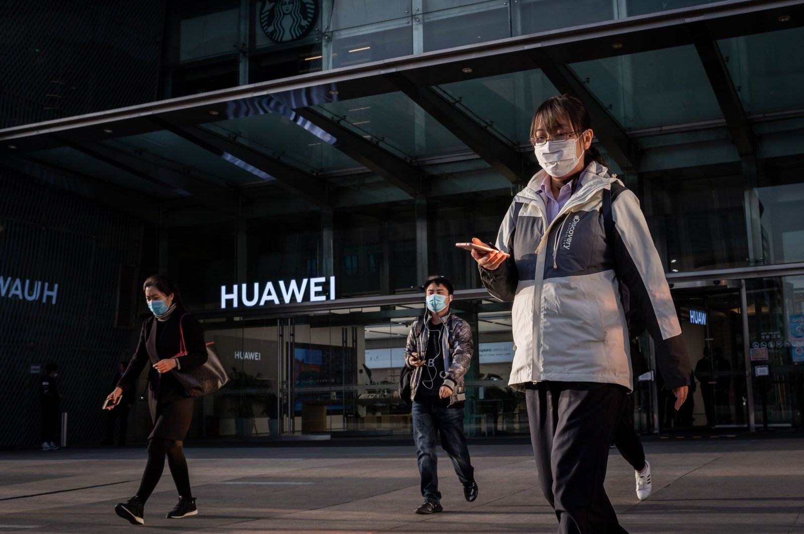 People wearing face masks as a preventive measure against COVID-19 walk outside a shopping mall past a Huawei shop in Beijing, Wednesday, April 1, 2020. (AFP Photo)