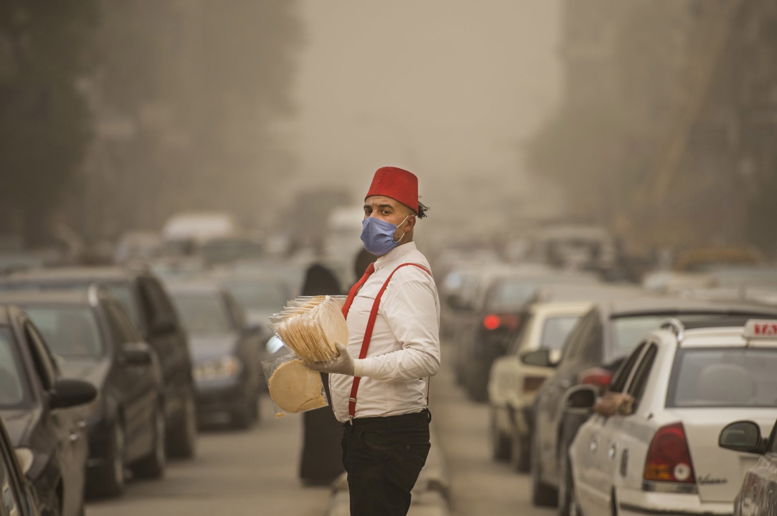 A street vendor wearing a protective face mask stands on a street between lines of cars during a sandstorm in Cairo, Egypt, Sunday, April 5, 2020. (EPA Photo)