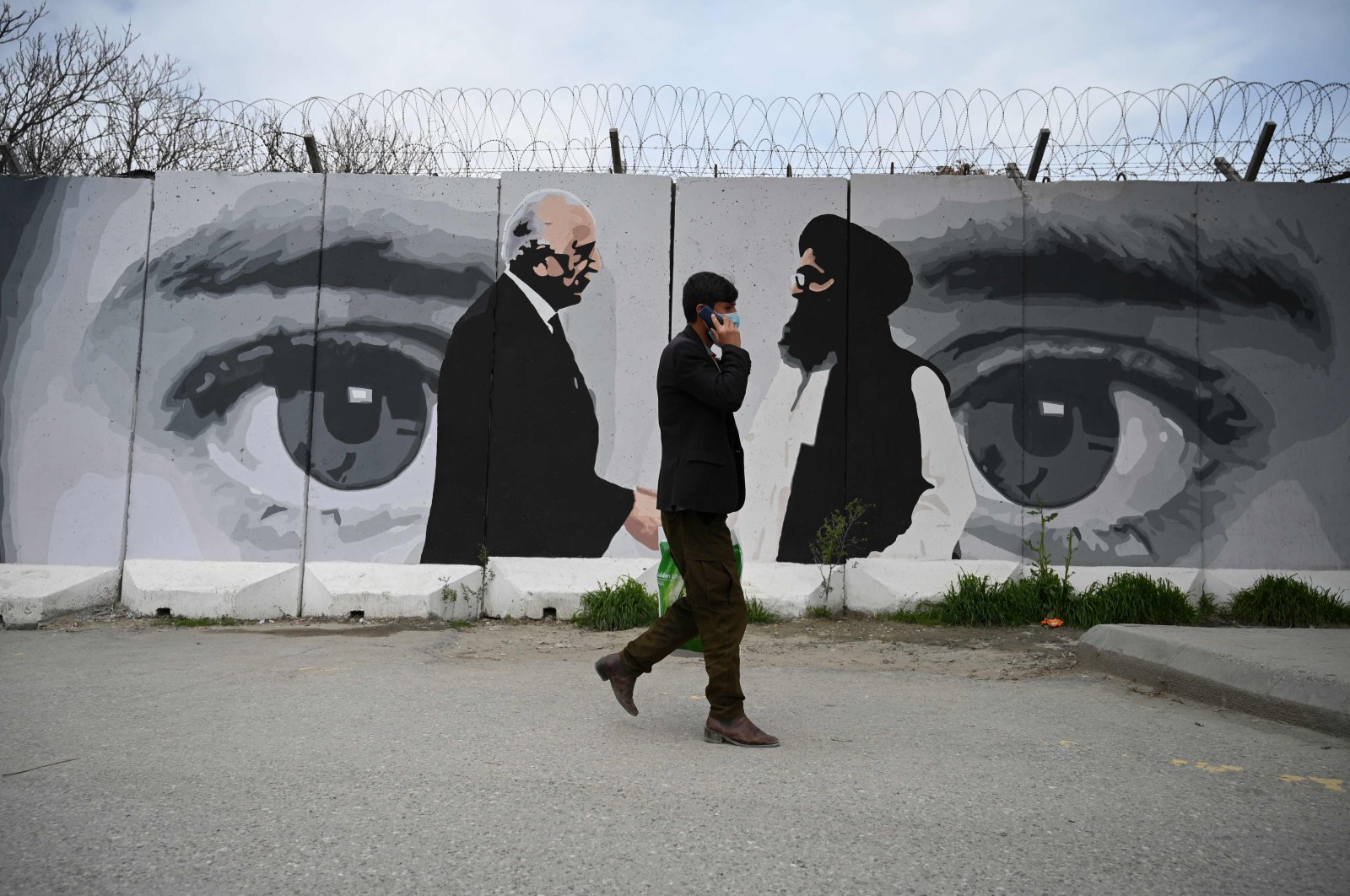 A man wearing a face mask walks past a wall painted with images of U.S. Special Representative for Afghanistan Reconciliation Zalmay Khalilzad (L) and Taliban co-founder Mullah Abdul Ghani Baradar (R), in Kabul, Sunday, April 5, 2020. (AFP Photo)