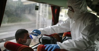 A health official measures the body temperature of a passenger on a bus at a check point, Istanbul, Sunday, March 29, 2020. (AP Photo)