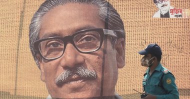 A policeman wearing a facemask amid fears of the spread of coronavirus walks past a banner with a picture of Bangladesh’s founder Sheikh Mujibur Rahman in Dhaka,  March 09, 2020. (AFP)