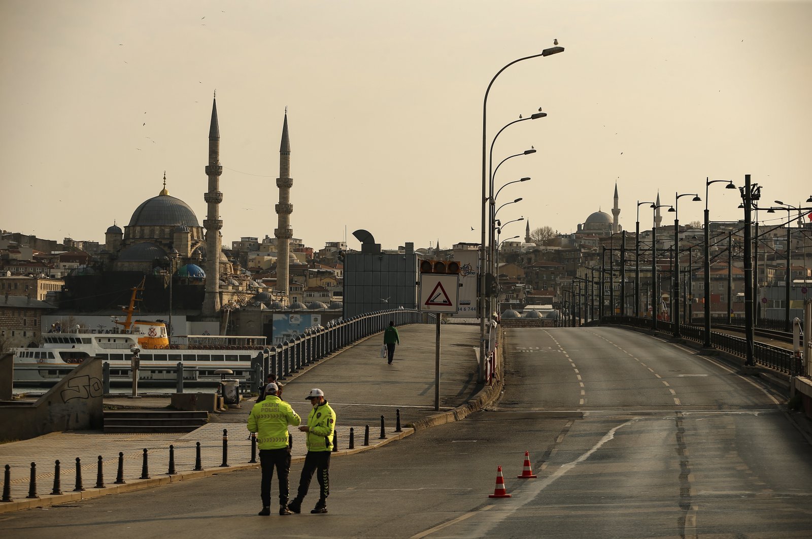 Police officers stand in the normally crowded but now mostly deserted Galata Bridge over Golden Horn with New Mosque in the background hours after the two-day curfew declared by the government to slow coronavirus spread, in Istanbul, Saturday, April 11, 2020. (AP Photo)