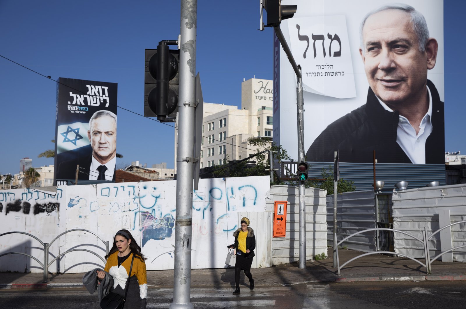 People walk next to election campaign billboards showing Israeli Prime Minister Benjamin Netanyahu (R) and Benny Gantz (L), Bnei Brak, March 1, 2020. (AP Photo)