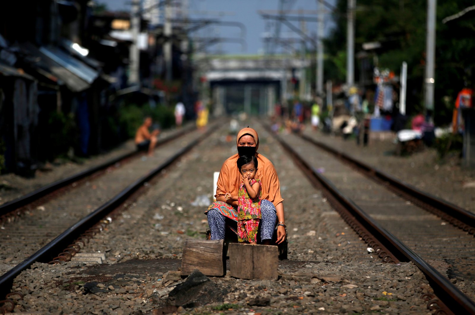A woman wearing a face mask and a child sit between rail tracks, during the imposition of large-scale social restrictions by the government to prevent the spread of the coronavirus disease in Jakarta, Indonesia, April 12, 2020. (Reuters Photo)