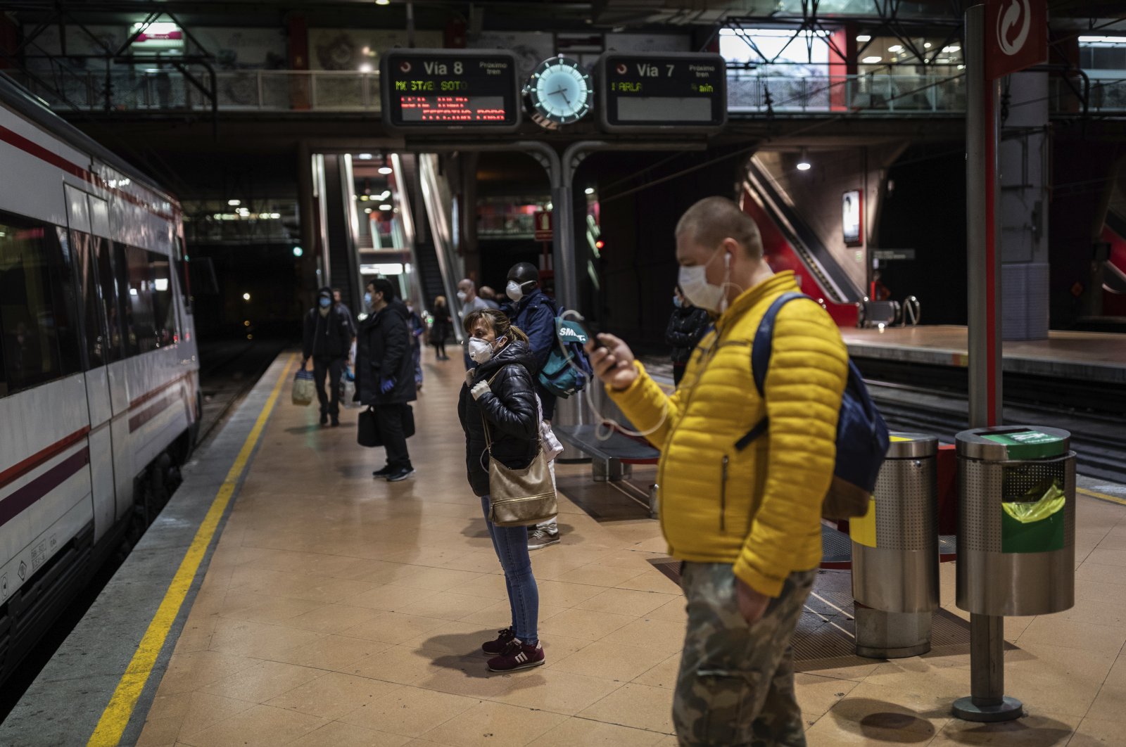 Commuters wear face masks to protect against the coronavirus while waiting on a platform at the Atocha train station, Madrid, April 13, 2020. (AP Photo)