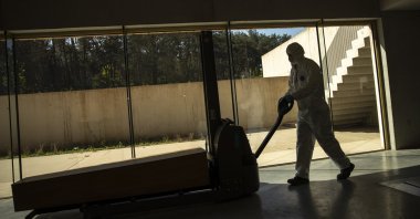 A worker, wearing full protective gear, moves a casket of a COVID-19 deceased at the Pontes crematorium and funeral center in Lommel, Belgium, Friday, April 10, 2020. (AP Photo)