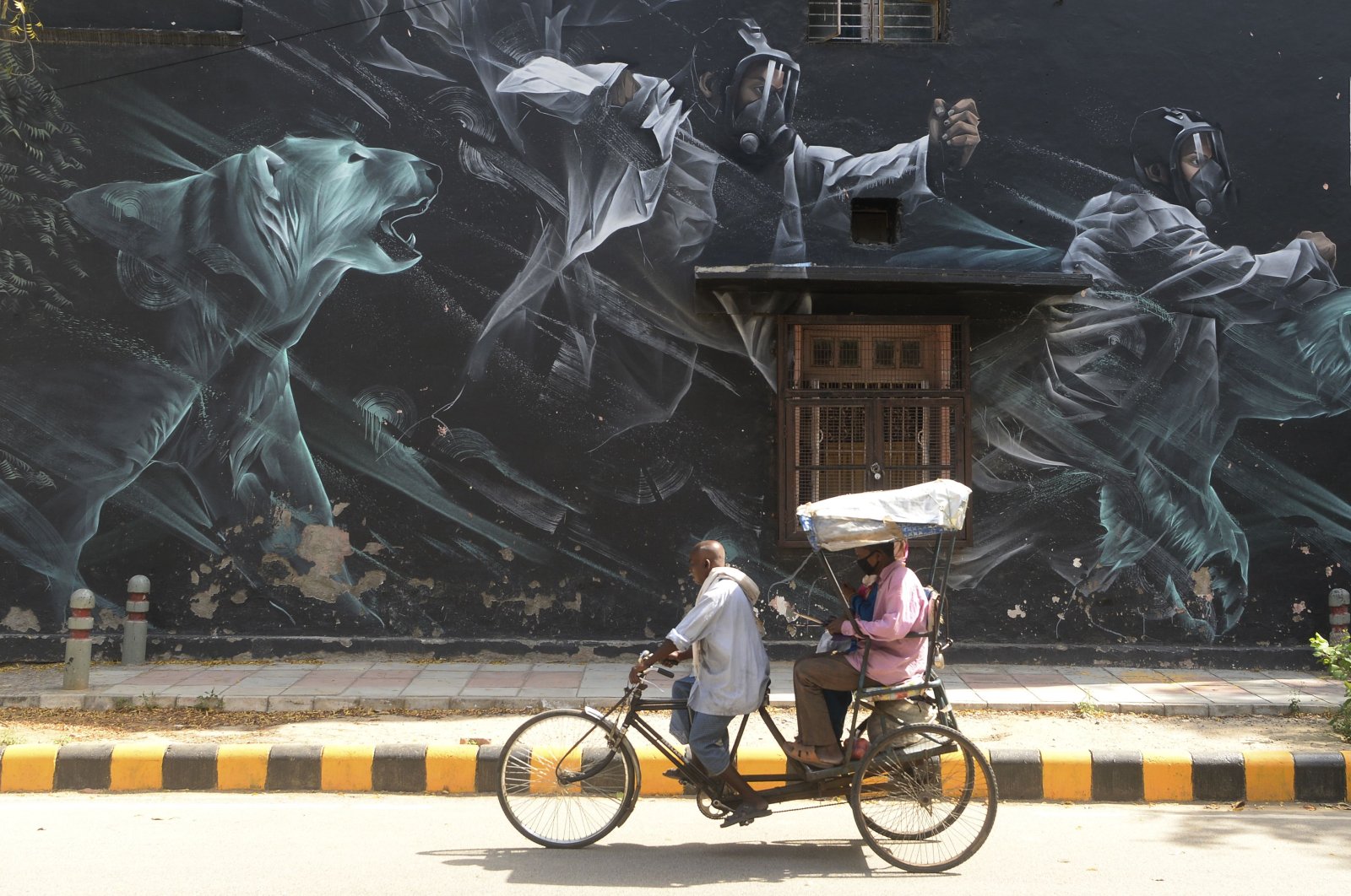A rickshaw driver carries passengers wearing facemasks past a mural at Lodhi Art District during a government-imposed nationwide lockdown as a preventive measure against the COVID-19 coronavirus, in New Delhi on April 13, 2020. (Photo by SAJJAD HUSSAIN / AFP)