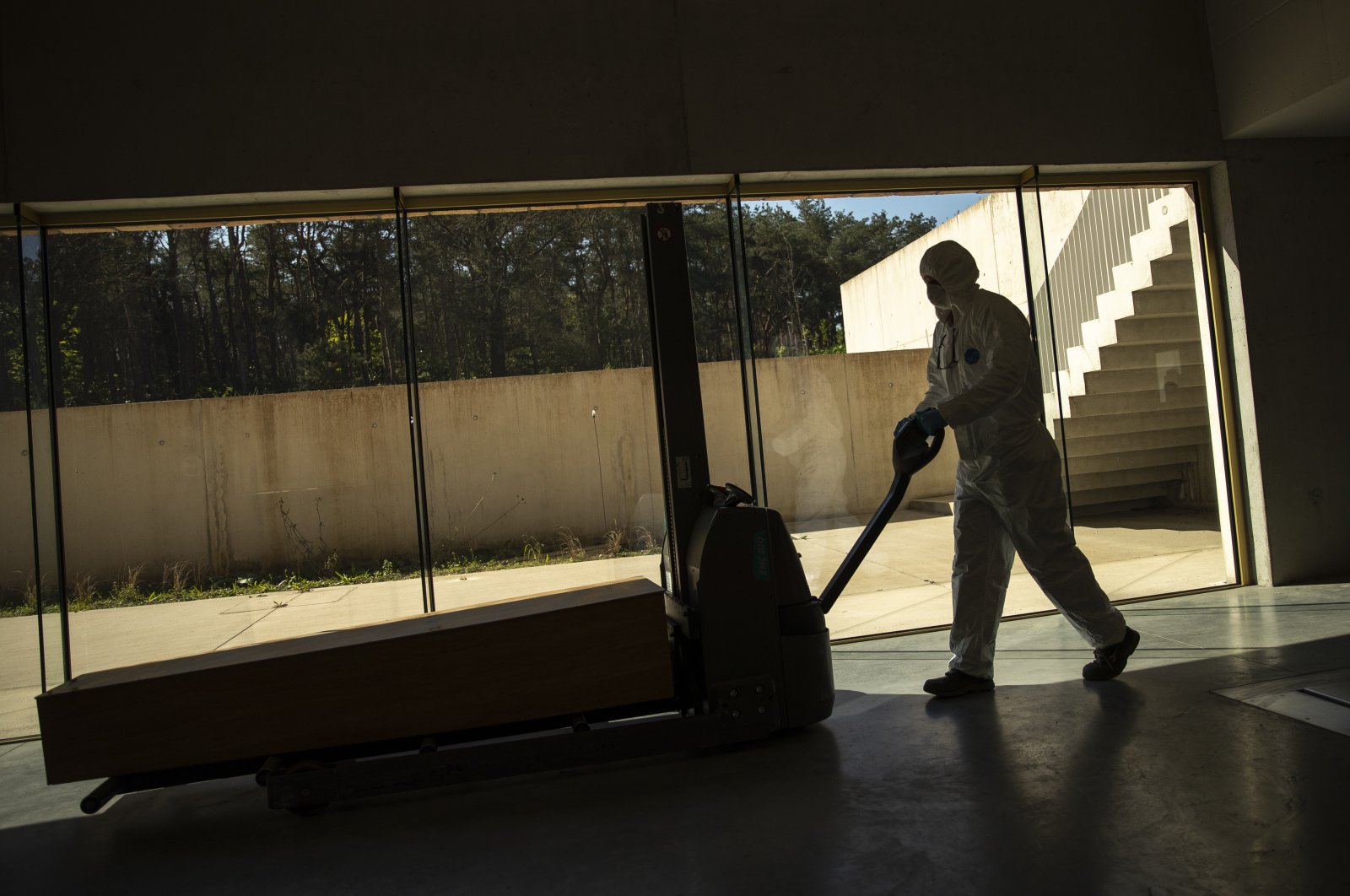 A worker, wearing full protective gear, moves a casket of a COVID-19 deceased at the Pontes crematorium and funeral center in Lommel, Belgium, Friday, April 10, 2020. (AP Photo)